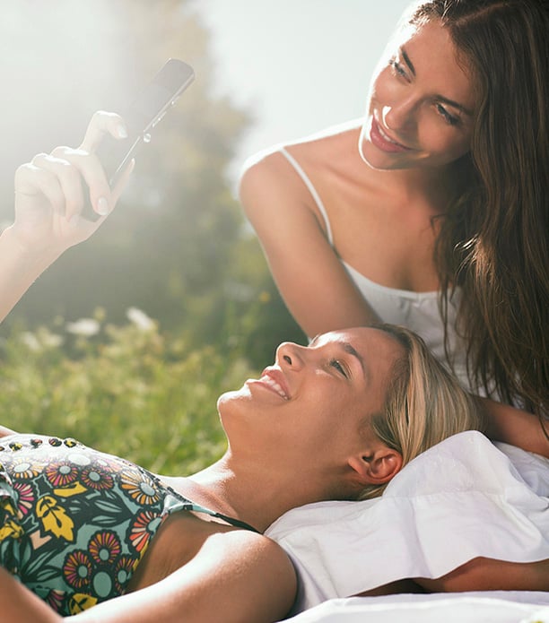 two woman sitting in meadow using mobile phone