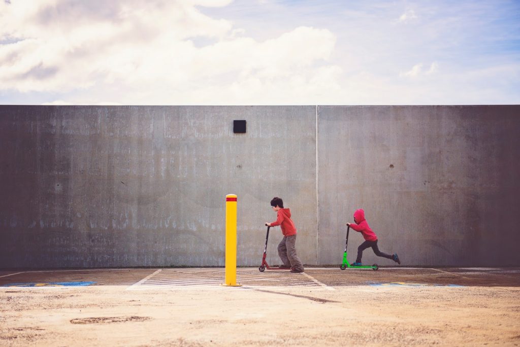 Dinâmicas para crianças: 3 ideias para fazer em casa 3 Crianças andando juntas de patinete como exemplo de dinâmica infantil