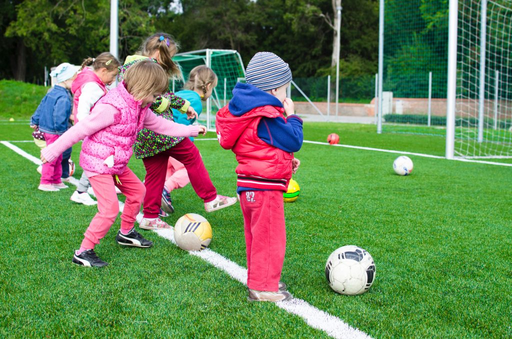 Crianças brincando em um campo de futebol, demonstrando a importância de compartilhar ideias na infância.