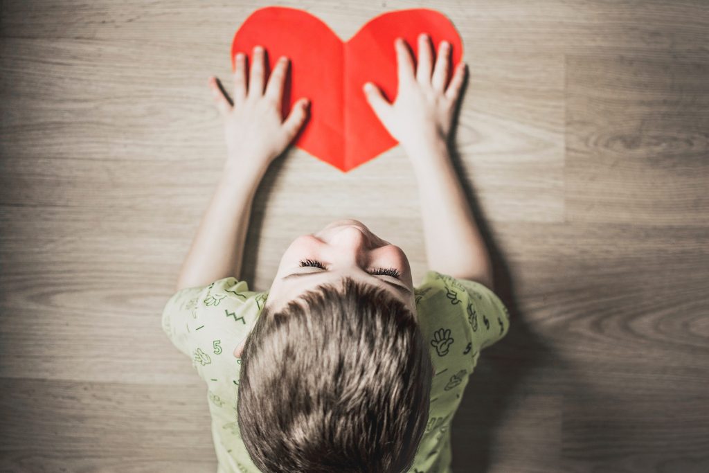 O que é psicomotricidade infantil e como promovê-la? 5 Visão aérea de um menino criança segurando um coração vermelho de papel, representando o papel da afetividade na psicomotricidade infantil.