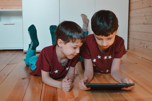 duas crianças deitadas no chão brincando com um tablet.