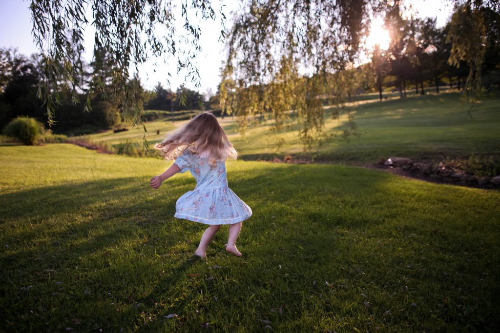 O que é psicomotricidade infantil e como promovê-la? 3 Criança menina dançando em um campo verde, demonstrando a importância da psicomotricidade infantil.