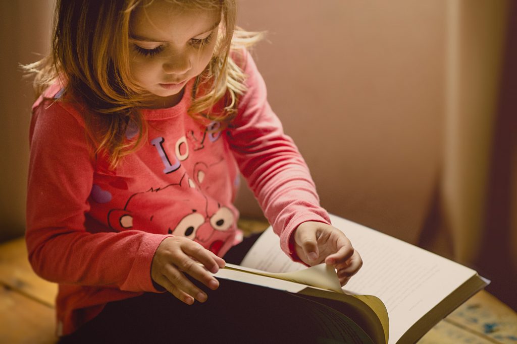 O que ajuda no desenvolvimento da criança? 1 Menina exemplificando o desenvolvimento da criança ao ler um livro.