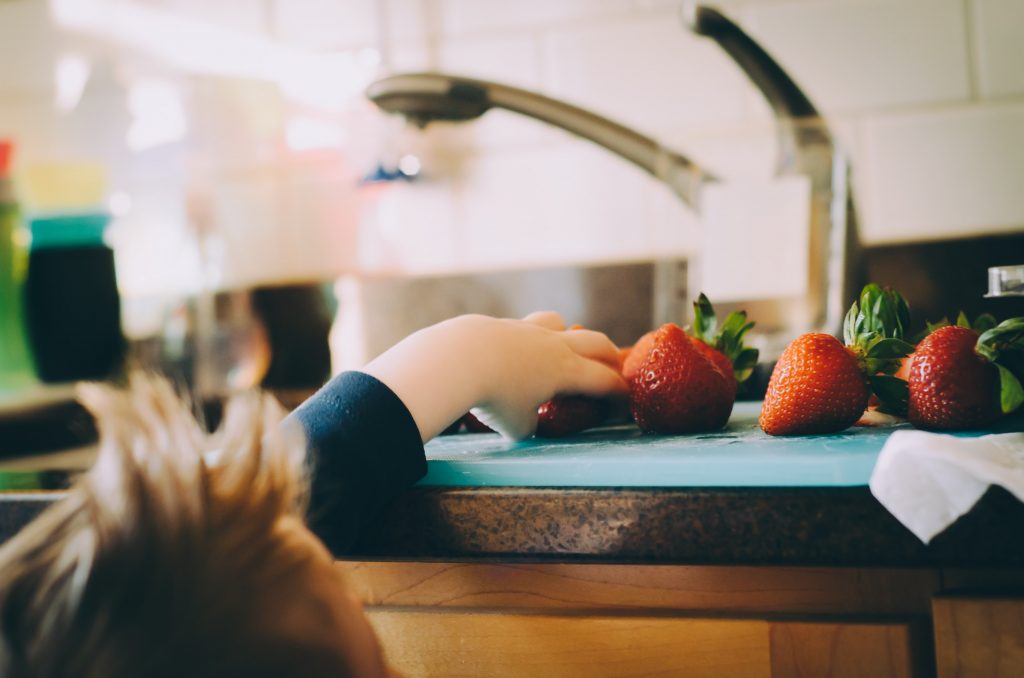 Criança pegando morangos na bancada da cozinha