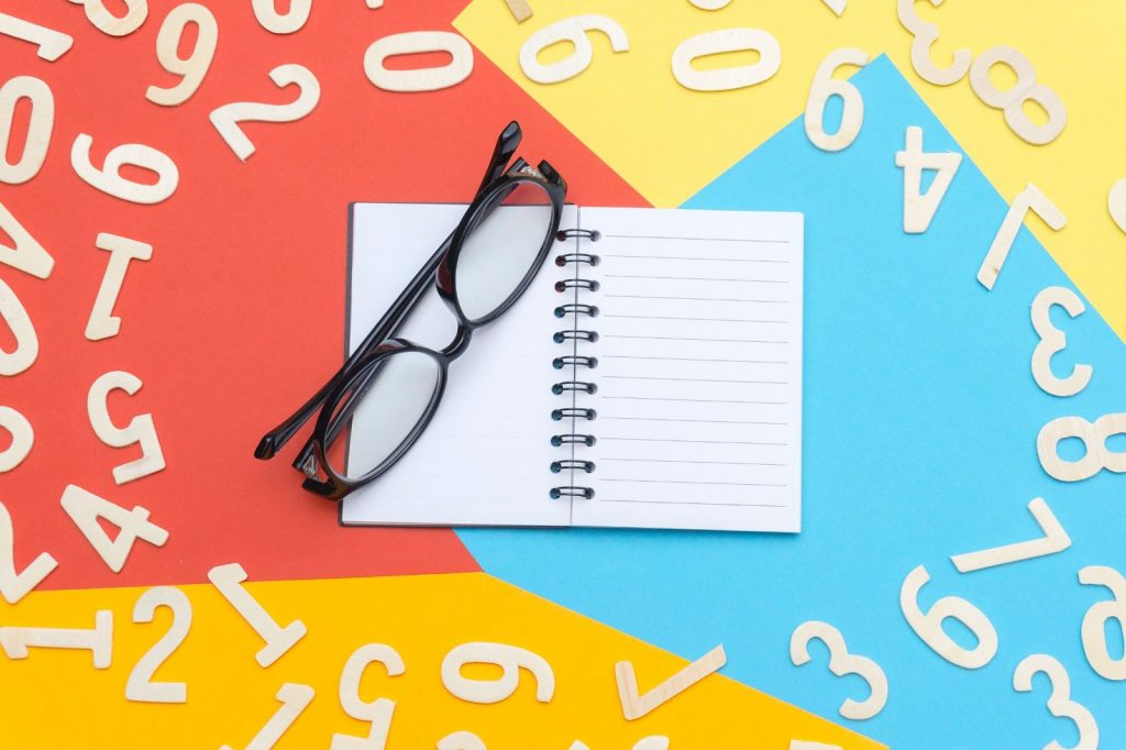 caderno em branco e um óculos em cima rodeados de números brancos
