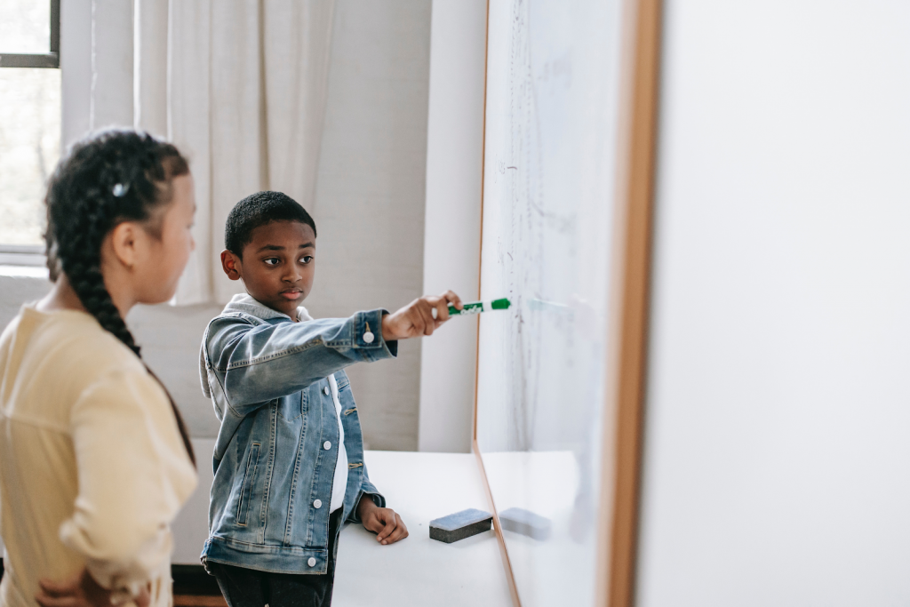 Uma das características do ensino por projetos são as dinâmicas que permitem a sociabilização e estimulam o engajamento. Na imagem, duas crianças discutem e escrevem seu projeto em uma lousa.