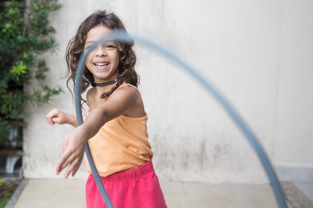 O que é psicomotricidade infantil e como promovê-la? 1 Criança menina desenvolvendo psicomotricidade infantil brincando com um bambolê.