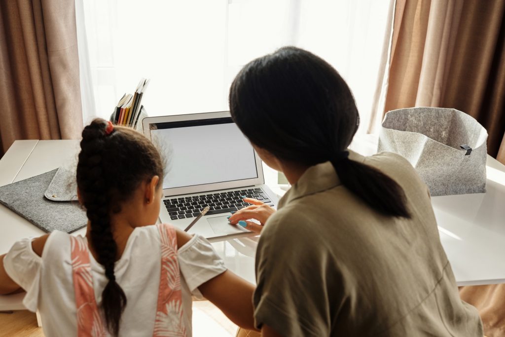 Na imagem, uma mãe participa ativamente da rotina de estudos da filha para ajudá-la com a motivação para estudar diariamente.