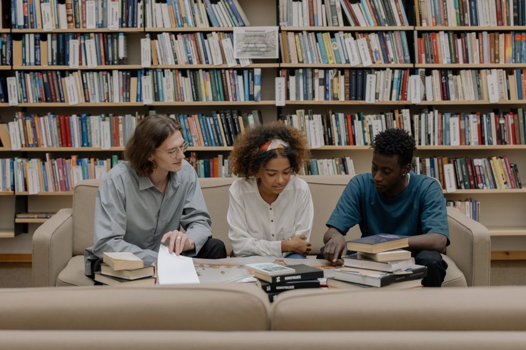 Na figura, três jovens estão em uma biblioteca, exercitando sua leitura em inglês.