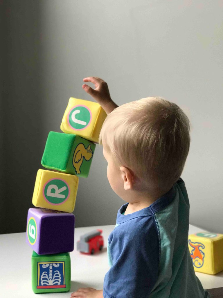 O que ajuda no desenvolvimento da criança? 5 Menino exemplificando o desenvolvimento da criança ao brincar com blocos de pelúcia.