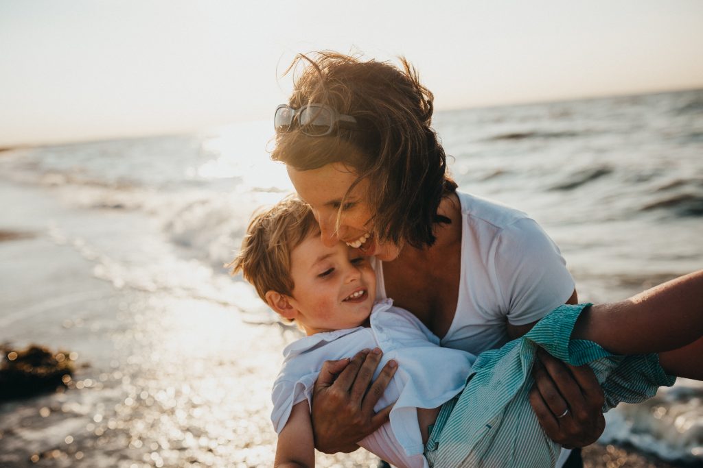 O que ajuda no desenvolvimento da criança? 7 Mãe brincando com seu filho no mar, exemplificando a importância do afeto no desenvolvimento da criança.