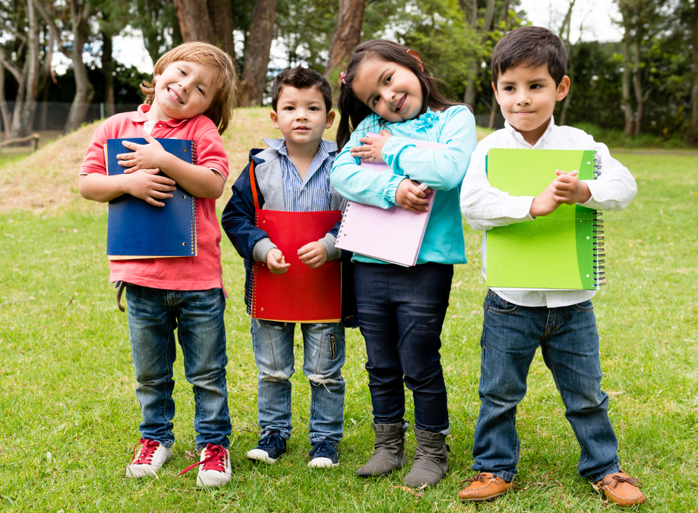 Happy group of school kids holding notebooks outdoors