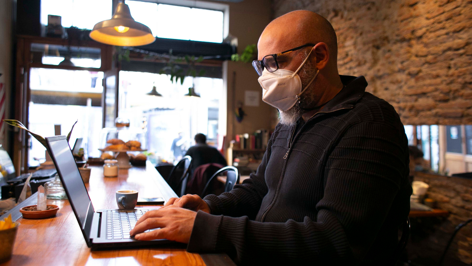 Hombre escribiendo en una computadora y sentado en un bar