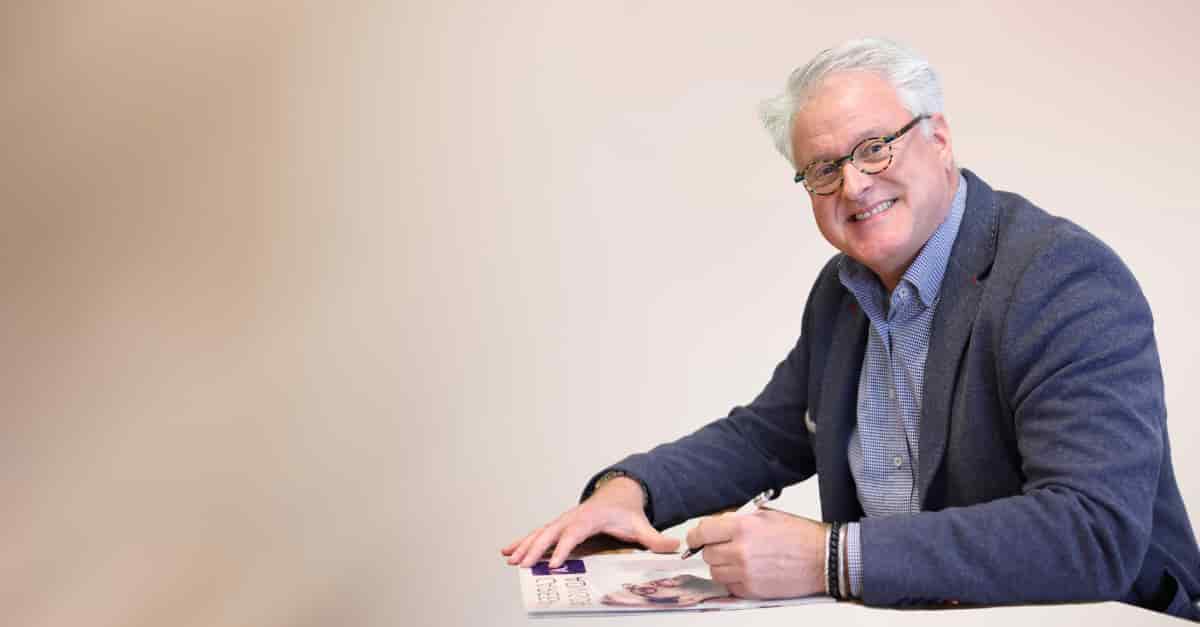 Coach René aan tafel met een pen in de hand en kijkend in de camera
